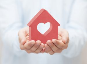 Hands holding a red house-shaped cutout with a heart in the center, symbolizing care in heat pump installation.