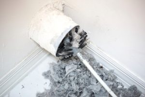 Air duct cleaning brush removing accumulated dust and debris from a vent, with loose lint on the floor.