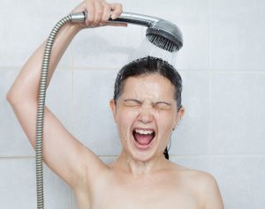 Woman reacting to cold water in the shower, possibly due to water heater maintenance issues.