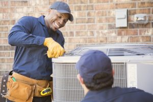 Two HVAC technicians performing ac installation outdoors with tools and protective gloves.
